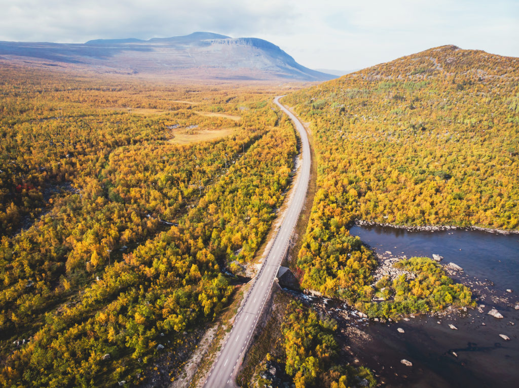 Aerial sunny fall autumn view of Abisko National Park, Kiruna Municipality, Lapland, Norrbotten County, Sweden, shot from drone, with Abiskojokk river, road and Nuolja mountai