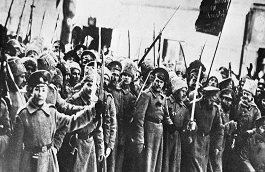 Historical photo depicts a crowd, possibly protesting, with some holding rifles or sticks and banners in the background.