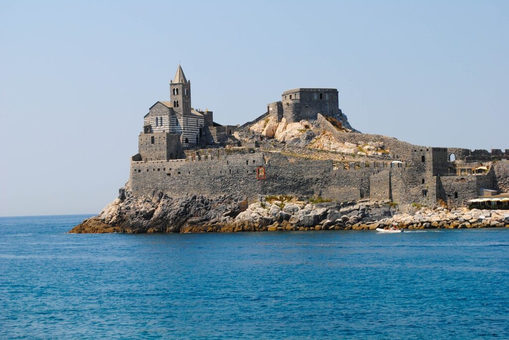 A coastal fortress with a church and tower on a clear day, overlooking a calm sea.