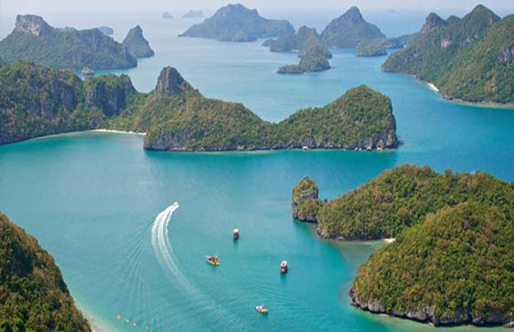 Aerial view of a tropical archipelago with emerald green waters, several boats, and lush green islands.