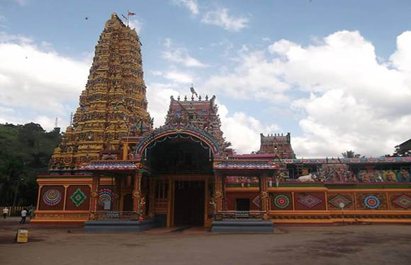 An image of a colorful Hindu temple with a tall gopuram (tower) adorned with intricate carvings and statues, under a cloudy sky.