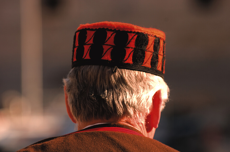 A person from behind wearing a traditional red hat with black patterns.