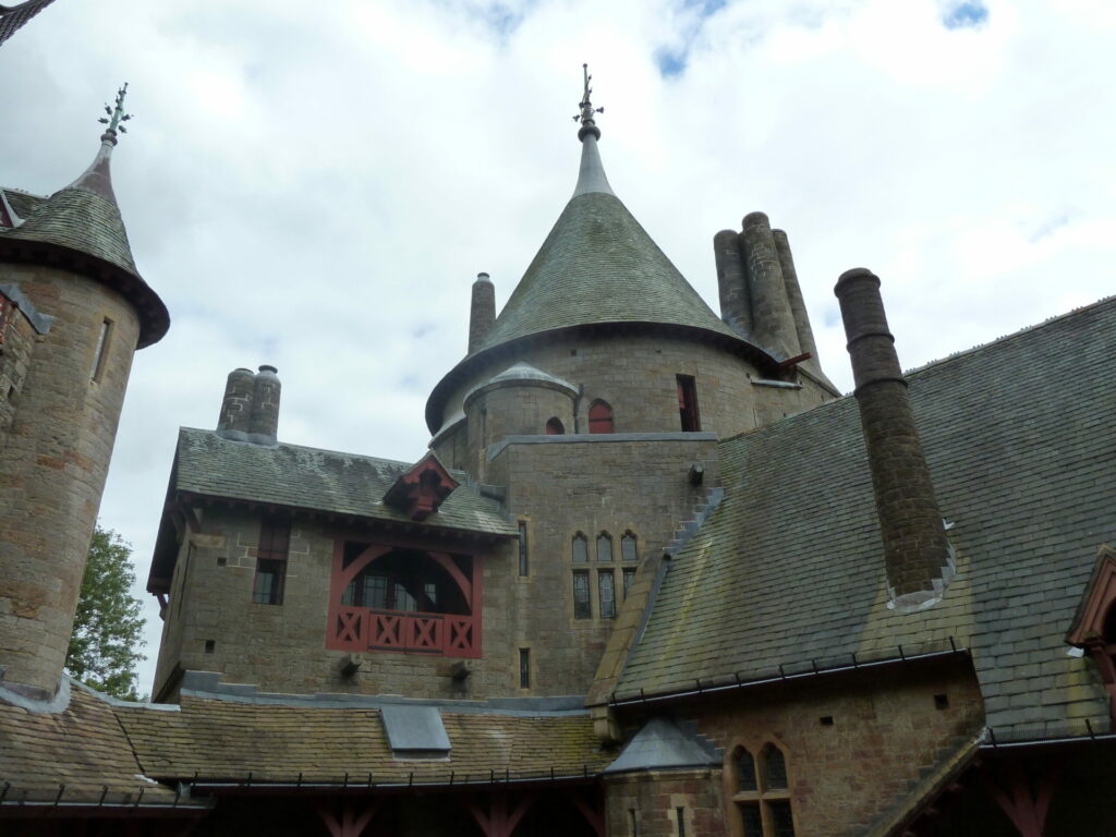 An image of a castle with conical roofs and a cloudy sky in the background.