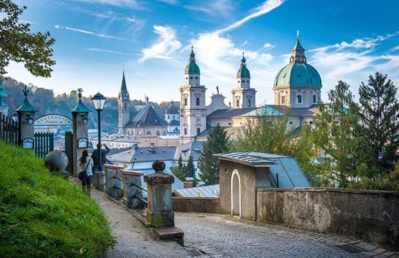 A picturesque view of a historic city with baroque architecture, viewed from a pathway at dawn or dusk under a clear sky.