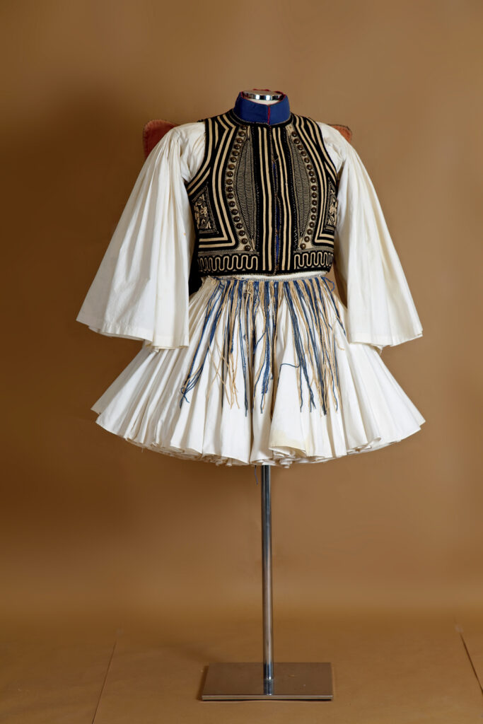 A traditional white dress with decorative black and gold patterns displayed on a mannequin against a plain background.