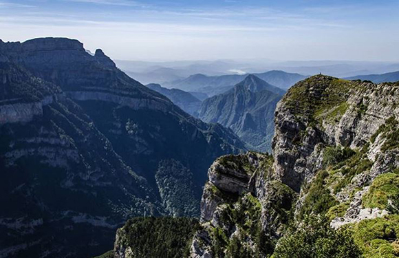 A scenic view of a mountainous landscape with steep cliffs and valleys, under a clear sky.