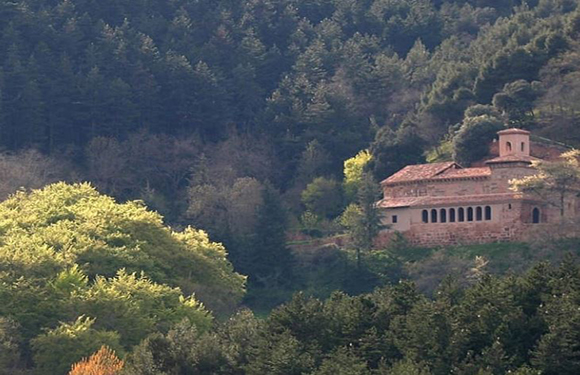 A small, traditional building with a terracotta roof nestled among lush green trees in a forested area.