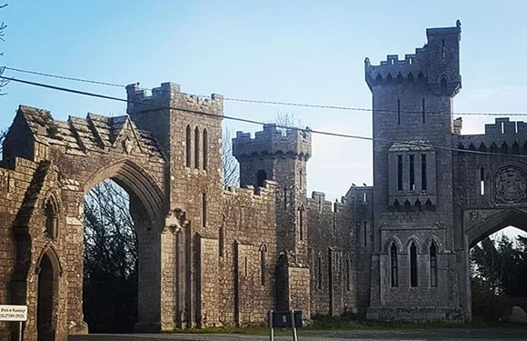 An image of a large, gothic-style stone structure with arches and towers, resembling a castle or fortress, under a clear sky.