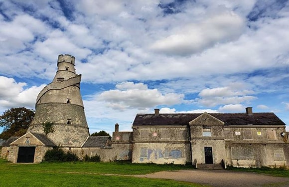 An image of an old, dilapidated building with a unique, large chimney structure under a partly cloudy sky.