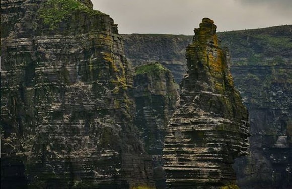 A photo of the Cliffs of Moher in Ireland, showing the rugged cliff faces and a stack formation against an overcast sky.