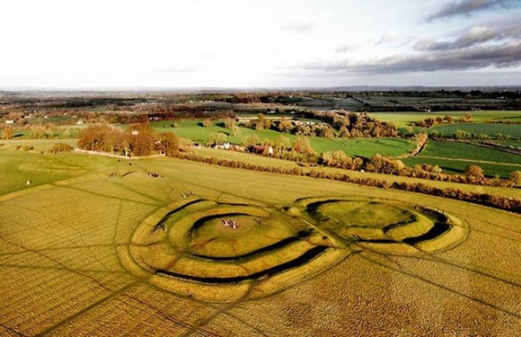 Aerial view of a large crop circle in a field with trees and a landscape in the background.