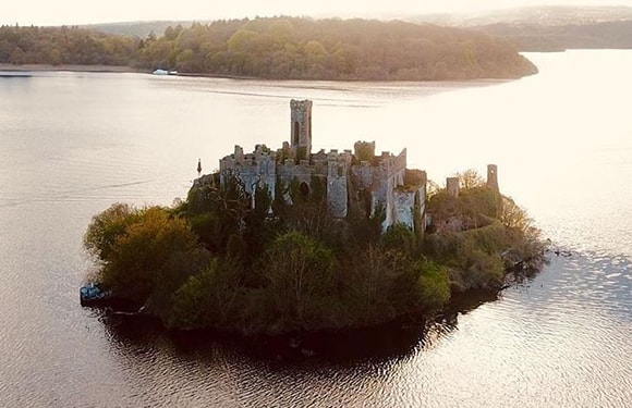 Aerial view of a ruined castle on a small island surrounded by water during daylight.