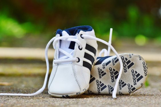 A pair of small Adidas branded shoes on a concrete surface.