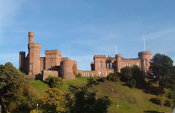 An image of a castle with cylindrical towers on a grassy hill under a clear blue sky.