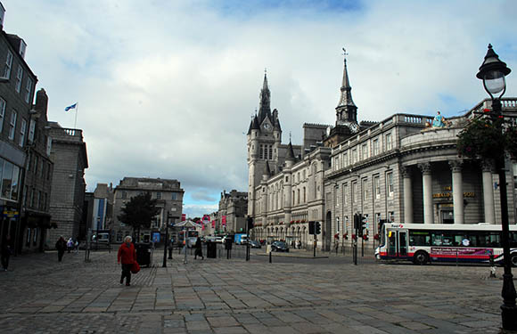 A city street scene with historical buildings, a cloudy sky, pedestrians, and a bus.