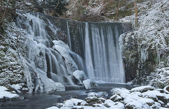 A waterfall with multiple cascades over a rocky cliff, surrounded by snow-covered vegetation.