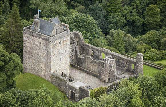 Aerial view of an ancient stone castle ruins surrounded by green trees.