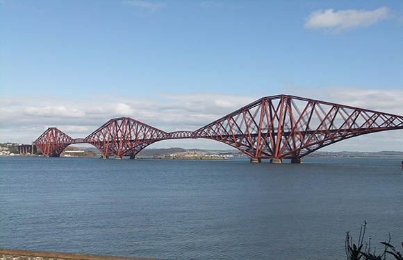 An image of the Forth Bridge, a cantilever railway bridge over a body of water, under a partly cloudy sky.