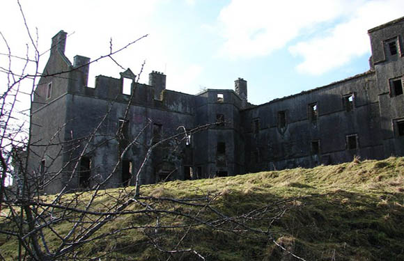 An image of a dilapidated castle with bare trees in the foreground and a partly cloudy sky in the background.