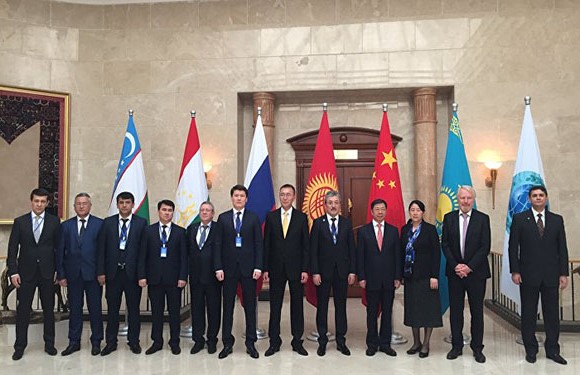 A group of individuals standing in a row inside a building, in front of flags from various countries.