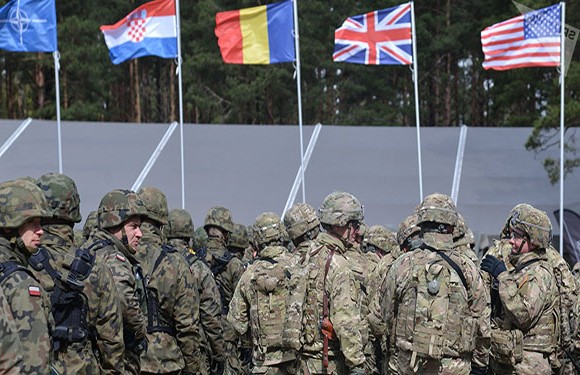 Soldiers in camouflage stand before national flags of Croatia, Sweden, UK, and the US.