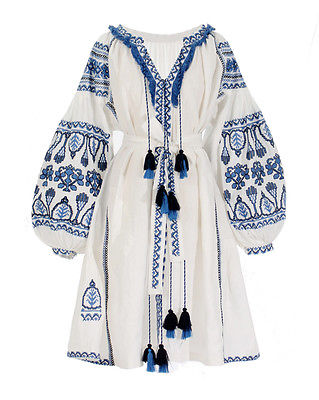 A white dress with blue embroidery and tassel details displayed against a plain background.