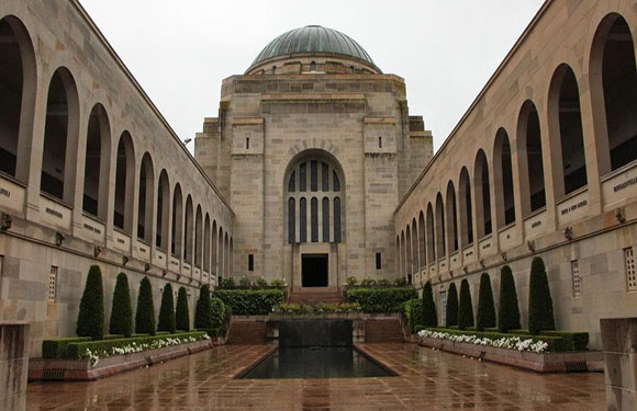 An image of a symmetrical building with a central dome, flanked by two colonnaded wings, and a rectangular reflecting pool in the foreground.