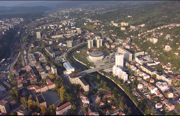 Aerial view of a city with buildings, trees, and a river, during daylight.