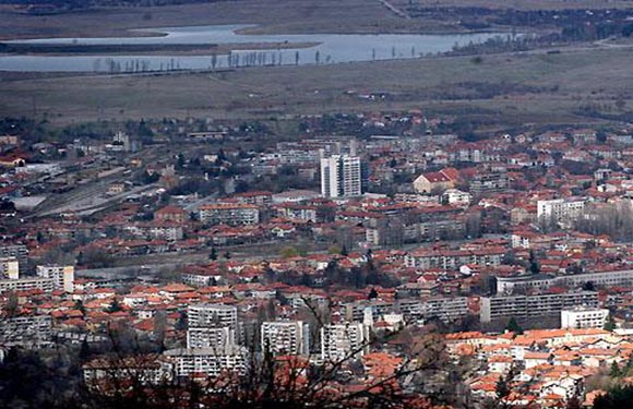 Aerial view of a densely populated city with numerous buildings and a body of water in the distance.