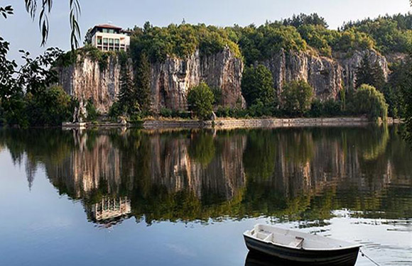 A serene lake with a reflection of a rocky cliff and trees on the water surface, and a small boat in the foreground.