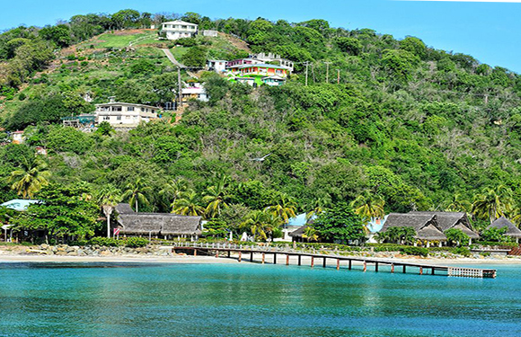 A coastal scene featuring a blue sea, a pier, thatched-roof structures on a beach, and a hill with colorful buildings.