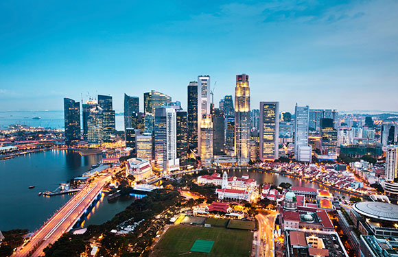 Aerial dusk view of a city with lit skyscrapers, a river, and densely packed, illuminated buildings.