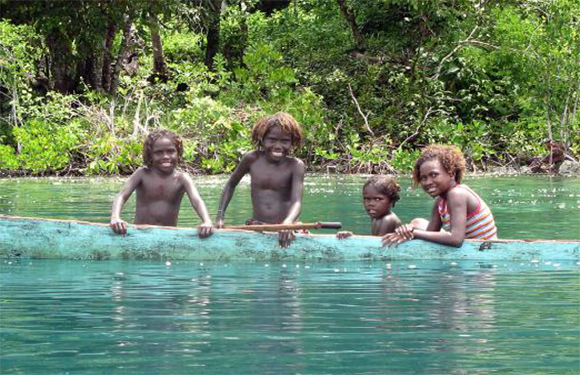 Four children in a canoe on a body of water with greenery in the background.