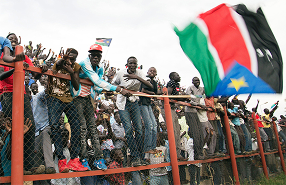 A group of people standing behind a fence, some waving flags, in an outdoor setting.