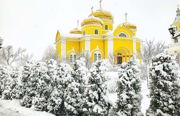 A yellow-domed church surrounded by snow-covered trees.