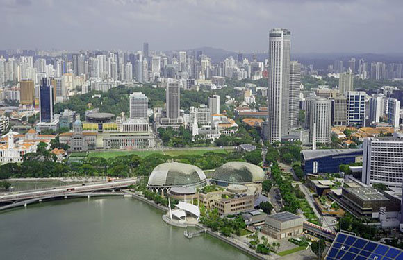 Aerial view of a modern cityscape with high-rise buildings, a river running through the area, and green spaces including two dome-shaped structures.