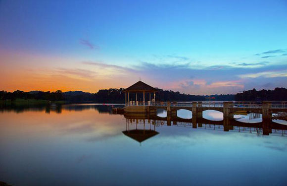 A serene lakeside view at dusk with a gazebo on a pier, reflecting on the calm water against a colorful sky.