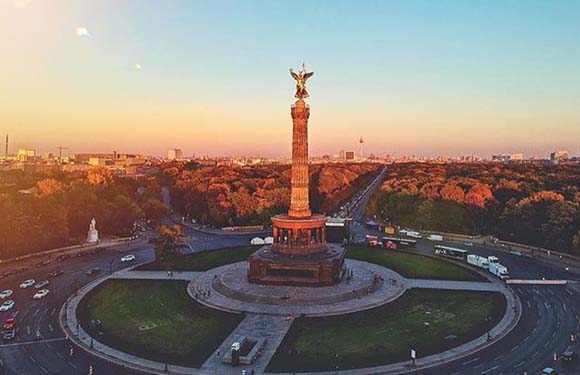 Aerial view of the Victory Column (Siegessäule) in Berlin at sunset with surrounding traffic circle and trees.