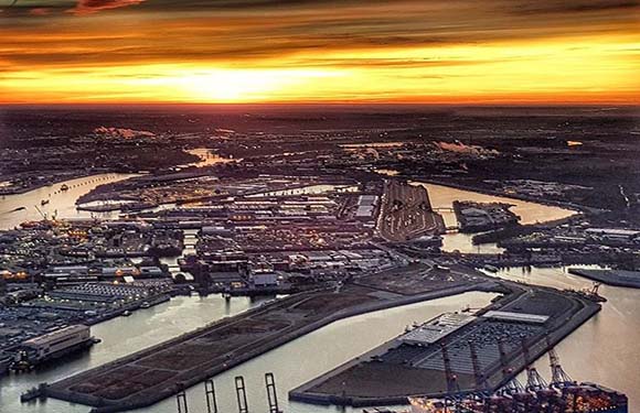 Aerial view of a port with numerous docks and waterways during sunset, featuring warm sky colors and urban infrastructure.