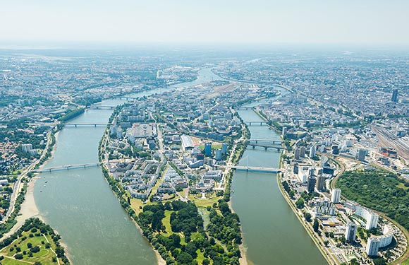 Aerial view of a city with a river curving through it, multiple bridges spanning the river, and a mix of green spaces and densely packed buildings.