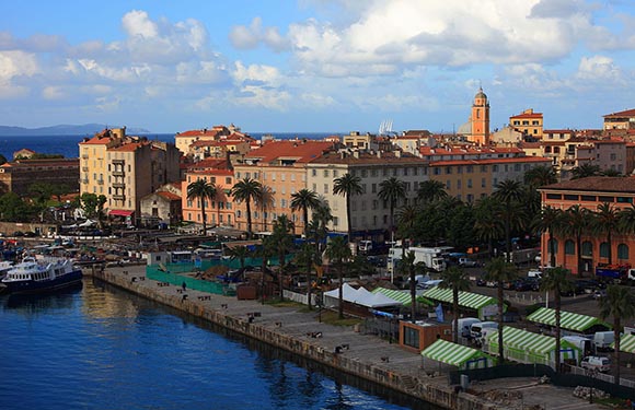 A coastal cityscape with buildings, a harbor with boats, and a clear sky with clouds.