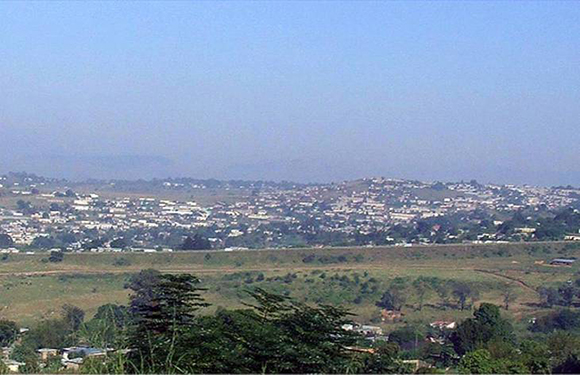 A panoramic view of a hilly suburban area with scattered buildings and vegetation under a hazy sky.