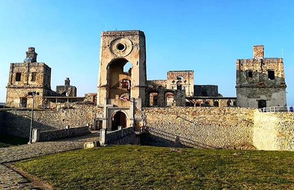 Ruins of an old stone fortress with archways and multiple levels under a clear sky.