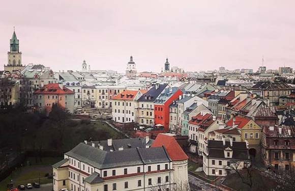 Aerial view of a European cityscape with historical buildings, various roof colors, and church spires under an overcast sky.