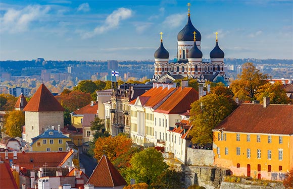 A picturesque historic town with traditional buildings, red roofs, and a prominent church with black domes under a blue sky.