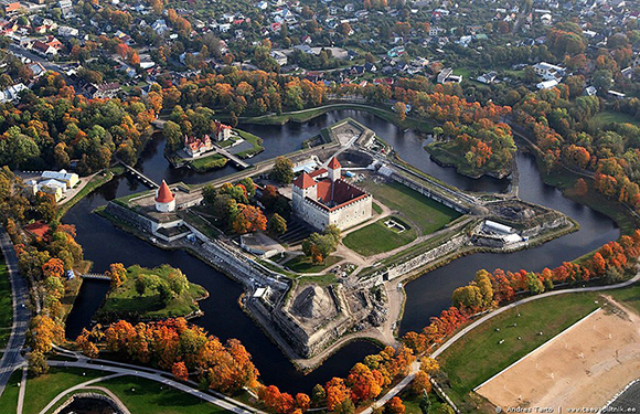 Aerial view of a star-shaped fortress surrounded by water with autumn-colored trees and roads nearby, in a town setting.