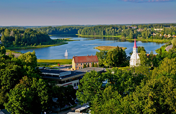 A picturesque view of a river, sailboat, lush trees, buildings, and a church spire.