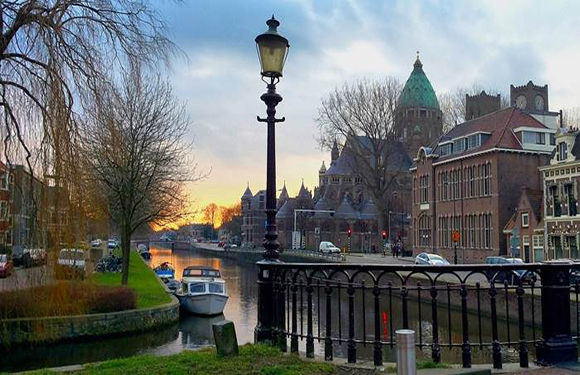 A scenic sunset view of an Amsterdam canal, featuring a bridge, street lamp, and historic buildings.