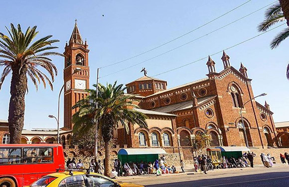 A photo shows people near a large brick church with a clock tower, under a clear sky. A red bus is on the left.