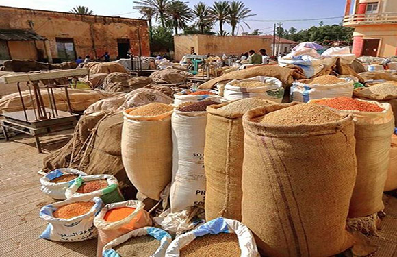 A variety of grains and spices in large open sacks displayed in an outdoor market setting.